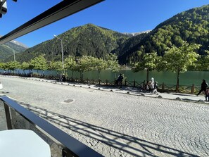A paved walkway along a lake with trees and mountains in the background. - Ozkan Hotel (Çaykara)