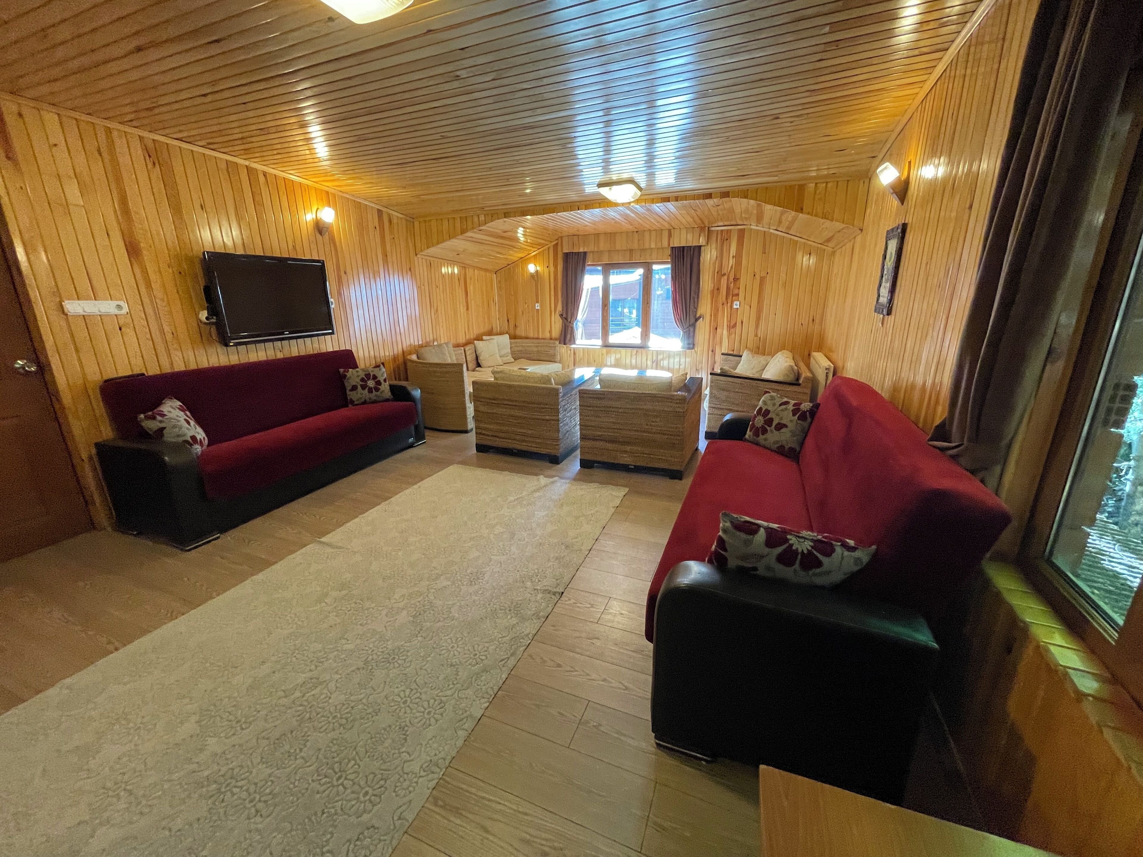 A cozy cabin interior with wooden walls, a red sofa, a beige sofa, and a small table.