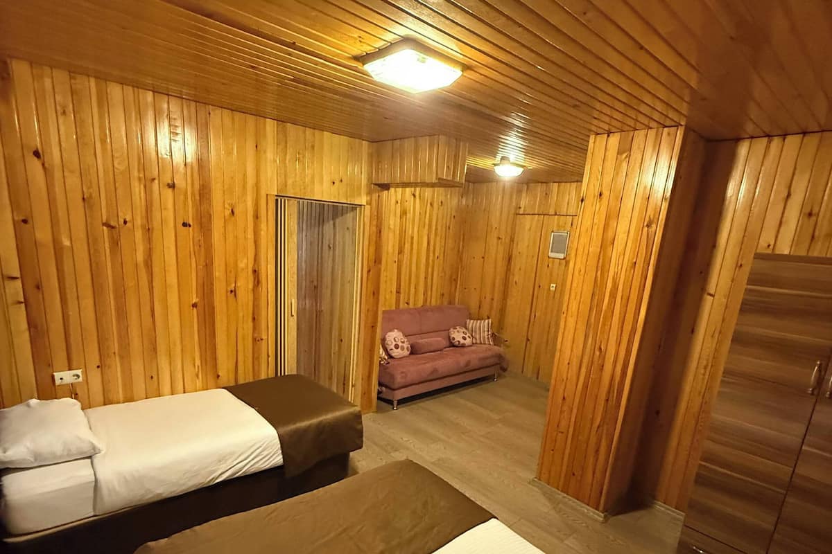 A room with wooden walls and ceiling, two beds, a sofa, and a wardrobe.