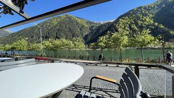 Um terraço à beira do lago com mesa e cadeiras, com vista para o lago e montanhas arborizadas.