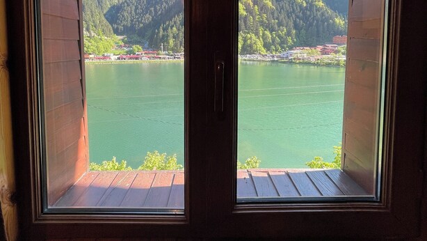 Habitación con dos ventanas que dan a un lago y montañas boscosas.