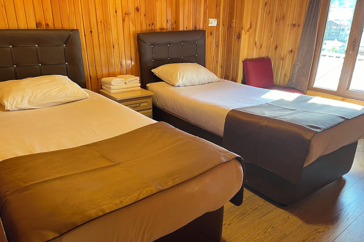 A room with two beds, wooden walls, a nightstand, and a window.
