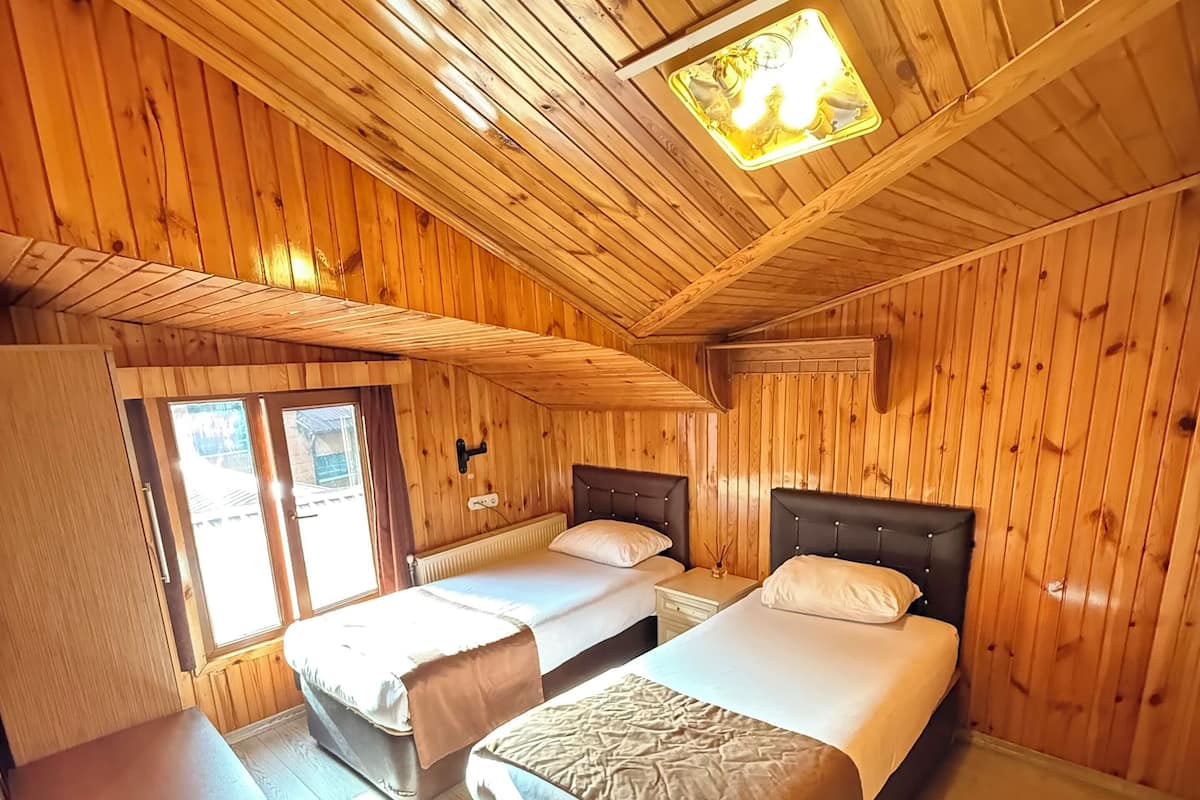 A cabin-style room with two beds, a chair, and a wooden ceiling.