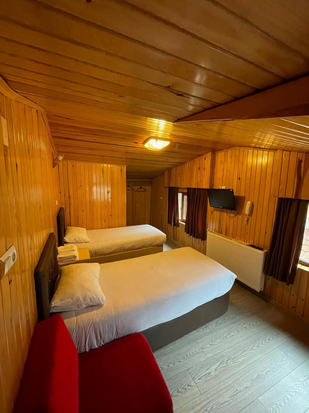 A wooden cabin room with two beds, a red chair, and a mounted TV.