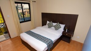 A neatly made bed with a wooden headboard, a bedside table with a lamp, and a window with curtains. - Hotel Dine & Dream (Kathmandu)