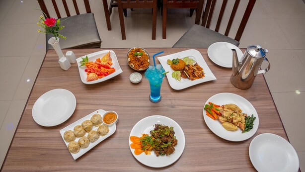 A dining table with various dishes, a blue drink with a straw, and a silver teapot. - Hotel Dine & Dream (Kathmandu)
