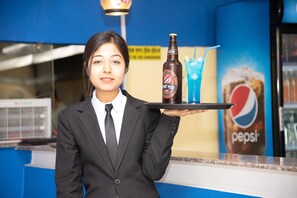 A person in a black suit holding a tray with a bottle and a glass.
