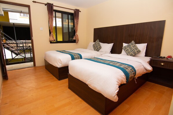 A hotel room with two beds, wooden flooring, a window with curtains, a nightstand, and a staircase leading to an outdoor area.