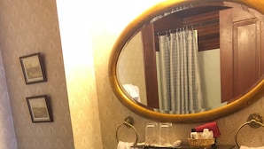 A bathroom with a round mirror, a sink, a towel rack, and a trash bin. - The Harry Packer Mansion Inn (Jim Thorpe)