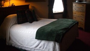 A neatly made bed with a white duvet and green throw, a bedside table with a lamp, and a dresser with drawers. - The Harry Packer Mansion Inn (Jim Thorpe)
