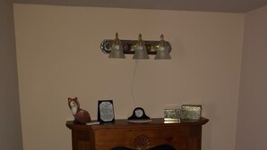 A cozy room with a wooden fireplace, a chair, a small table with a clock and decorative items, and a bookshelf with books. - The Harry Packer Mansion Inn (Jim Thorpe)