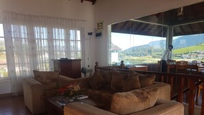 A cozy living room with a sofa, a coffee table with a vase, and a view of a golf course through large windows. - Villa lake view (Nuwara Eliya)