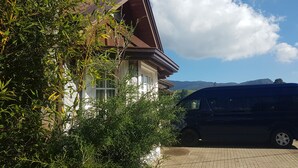 A house with a brown roof, surrounded by greenery, and a parked car in front. - Villa lake view (Nuwara Eliya)