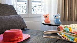 A room with a grey sofa, a small table with two bear figurines, a colorful fabric item, and a red hat on the sofa. - Hôtel 66 (Nice)