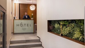 A hotel reception desk with a modern design, a receptionist, and a decorative wall with plants and a statue. - Hôtel 66 (Nice)