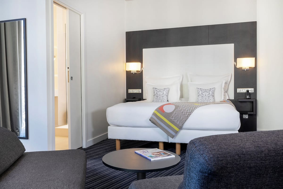 A hotel room with a bed, bedside tables, a round table with a magazine, and a sofa.