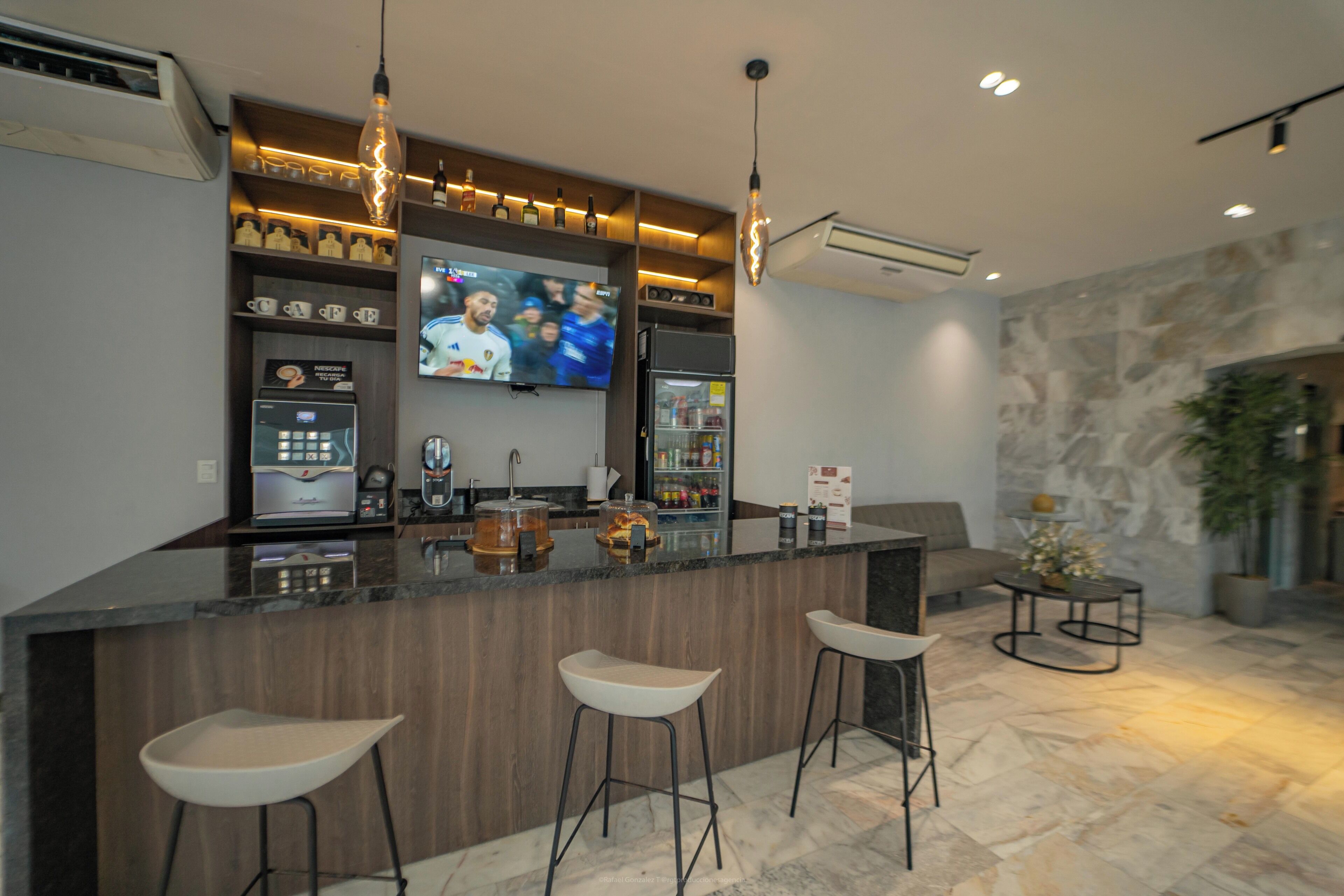 A modern kitchen with a bar area, bar stools, a television, and a stone wall.