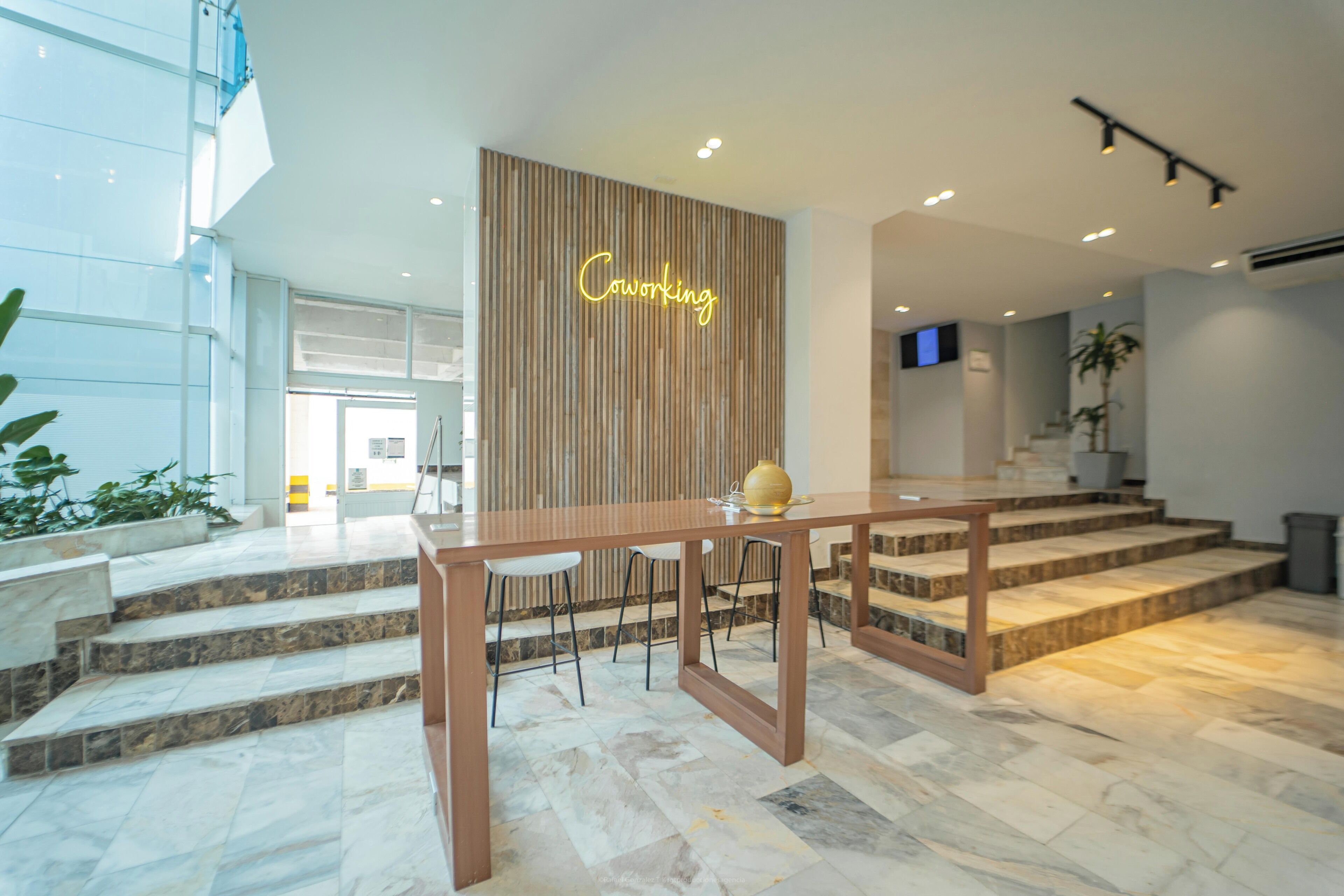 Et moderne interiør med en træreception, et skilt med teksten 'Coworking', marmorgulv og en trappe.