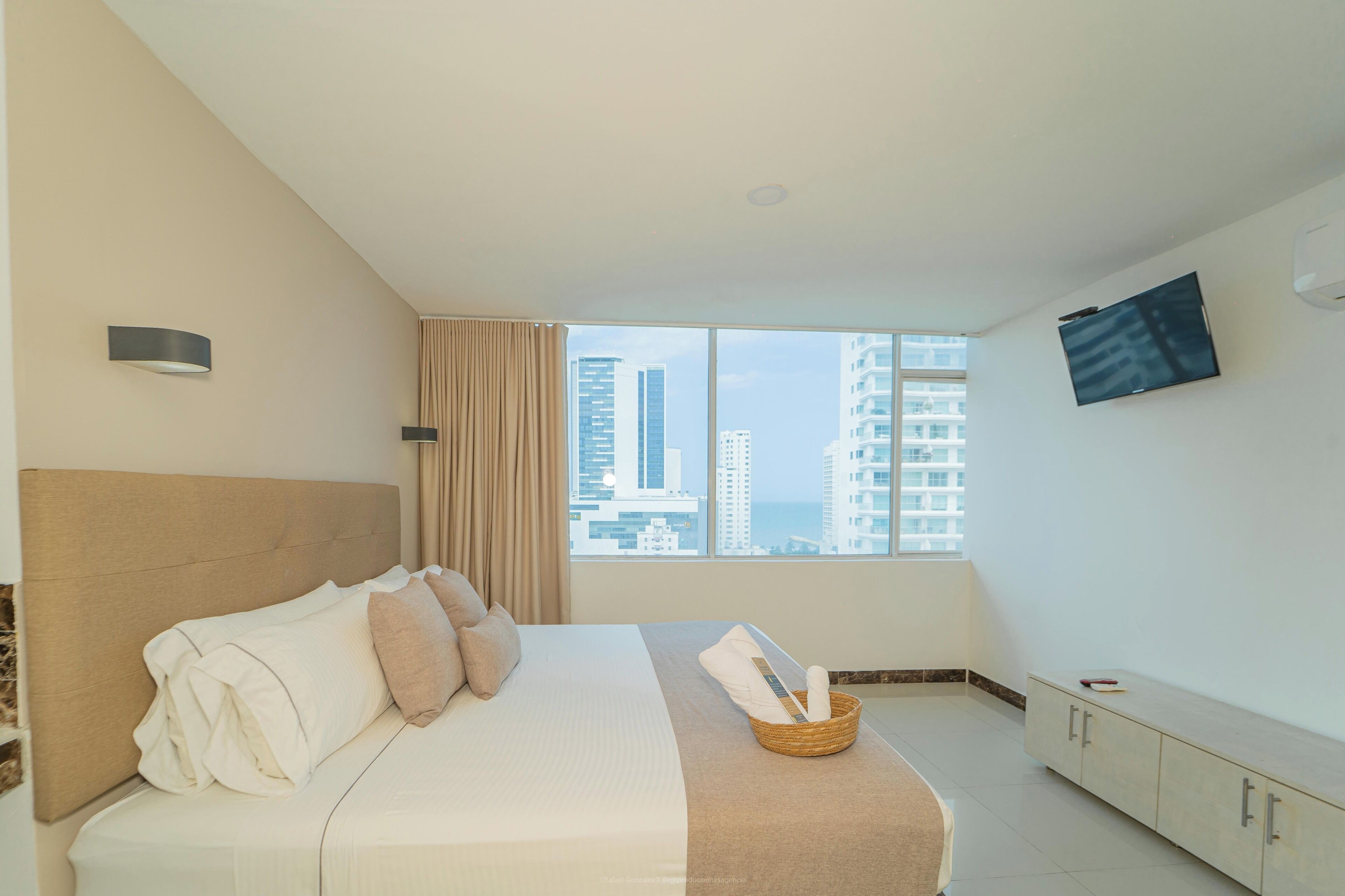 A hotel room with a bed, a television, a window with a city view, and a cabinet.