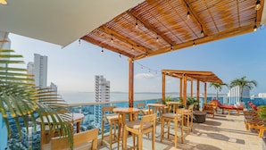 Eine Dachterrasse mit Holzmöbeln, einer Pergola und Blick auf Stadt und Meer.