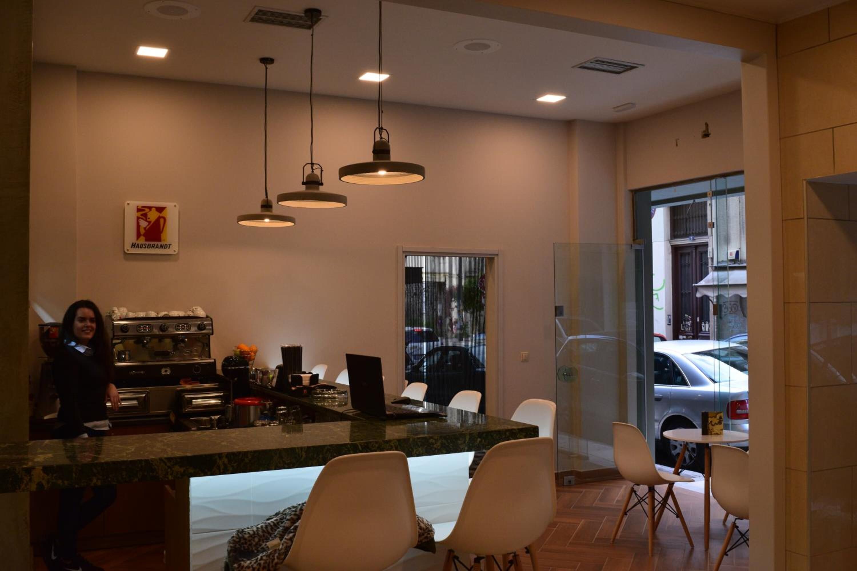 A modern kitchen area with a marble countertop, overhead pendant lights, and a coffee machine.