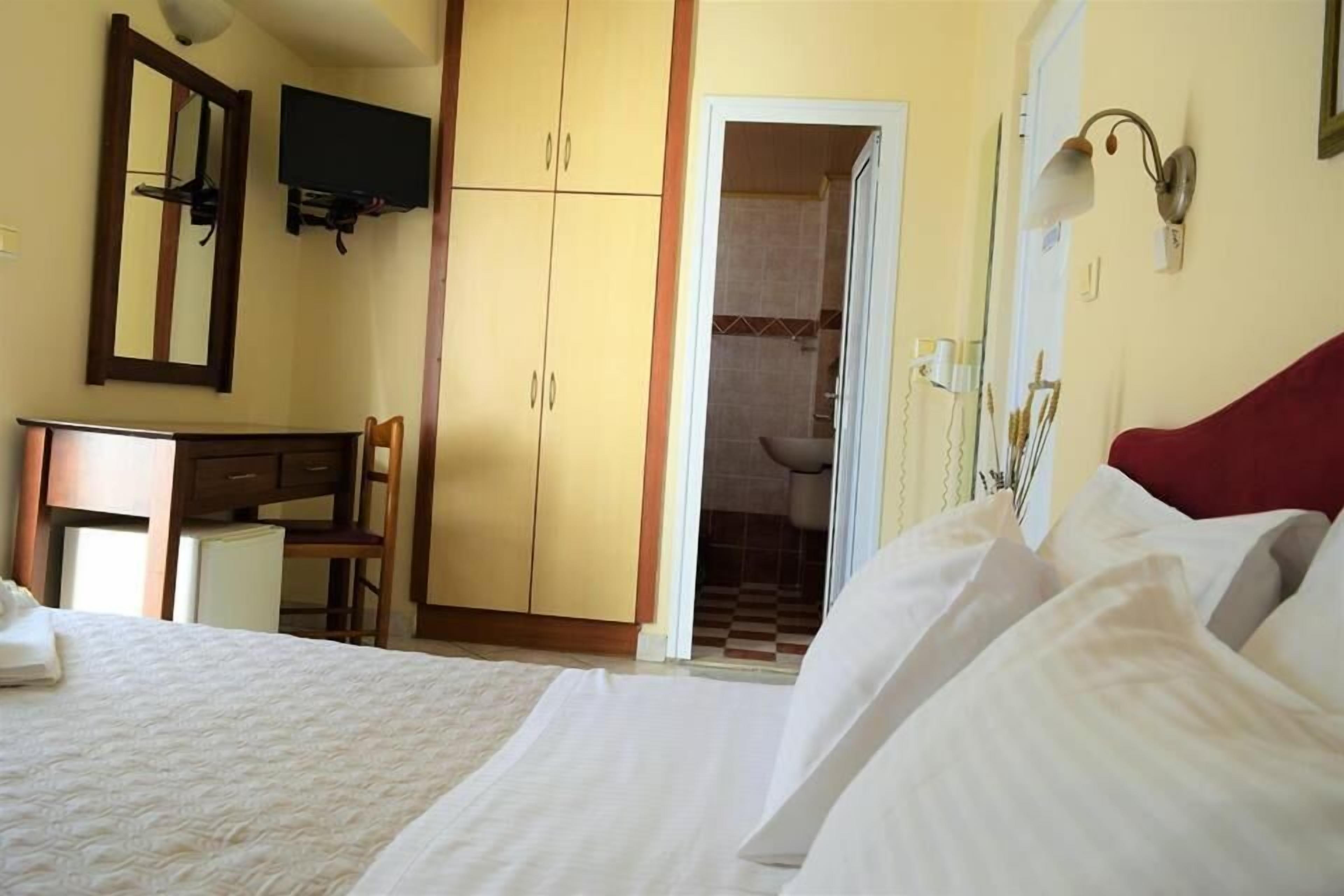 A hotel room with a bed, a desk, a chair, a television mounted on the wall, and a bathroom visible through an open door.