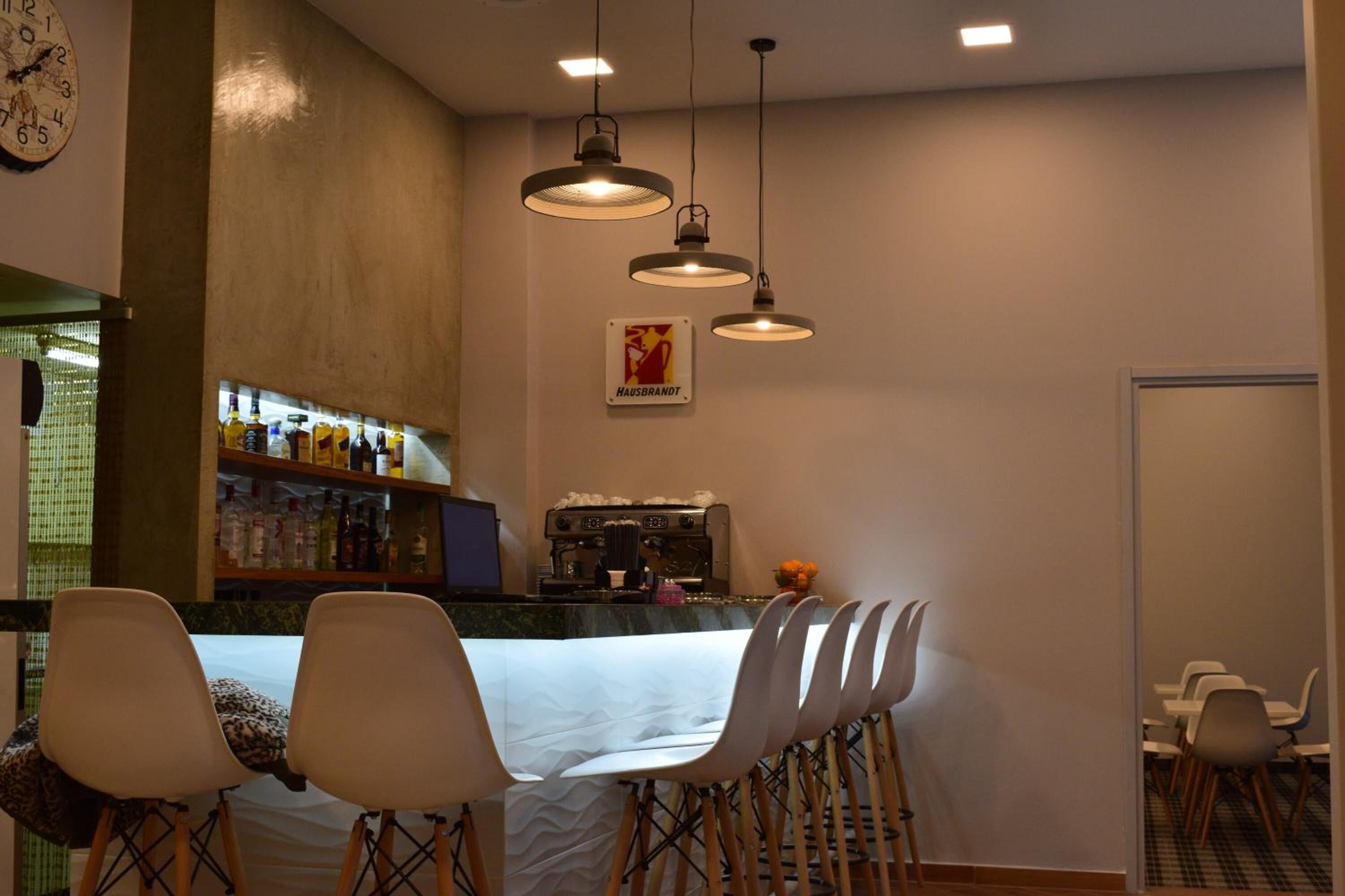 A bar area with a counter, shelves with bottles, and a coffee machine. There are chairs and a table in the foreground.