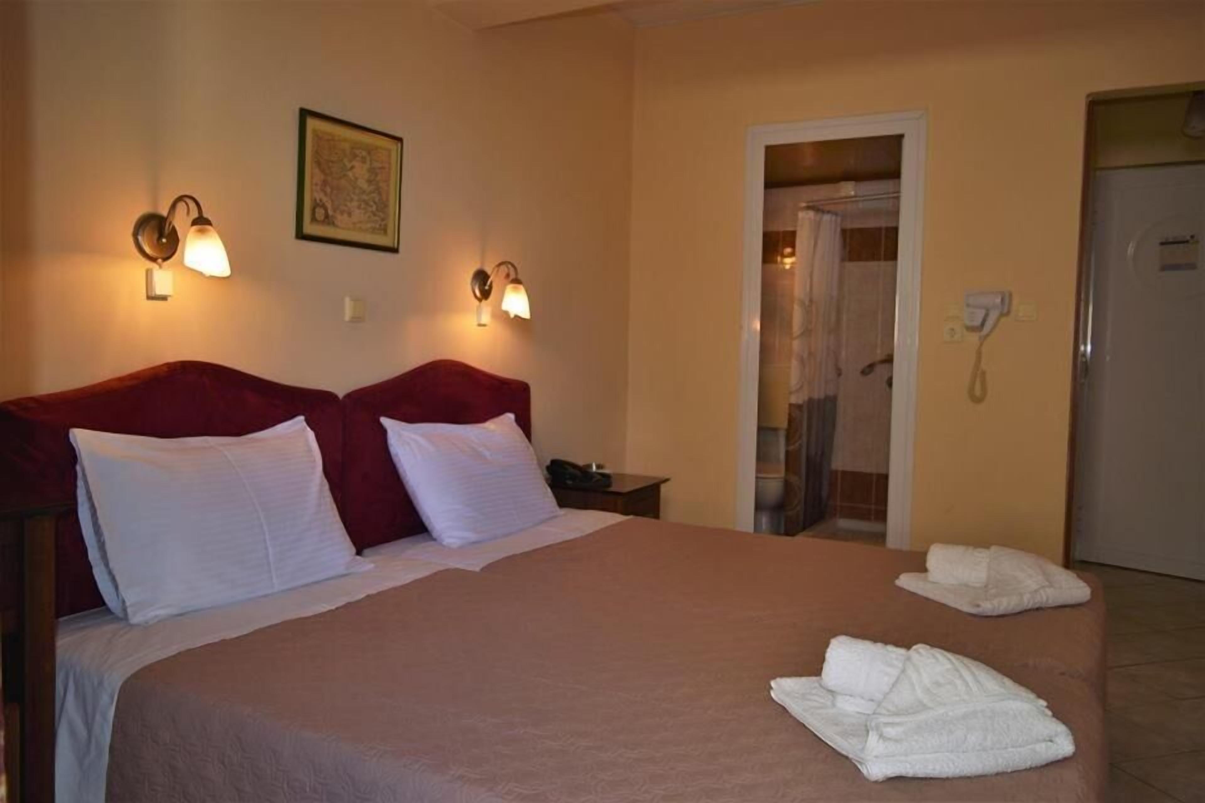 Quarto de hotel com uma cama grande, duas luminárias na parede, um mapa emoldurado, área de chuveiro e um telefone.