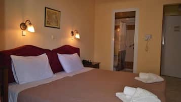 Quarto de hotel com uma cama grande, duas luminárias na parede, um mapa emoldurado, área de chuveiro e um telefone.
