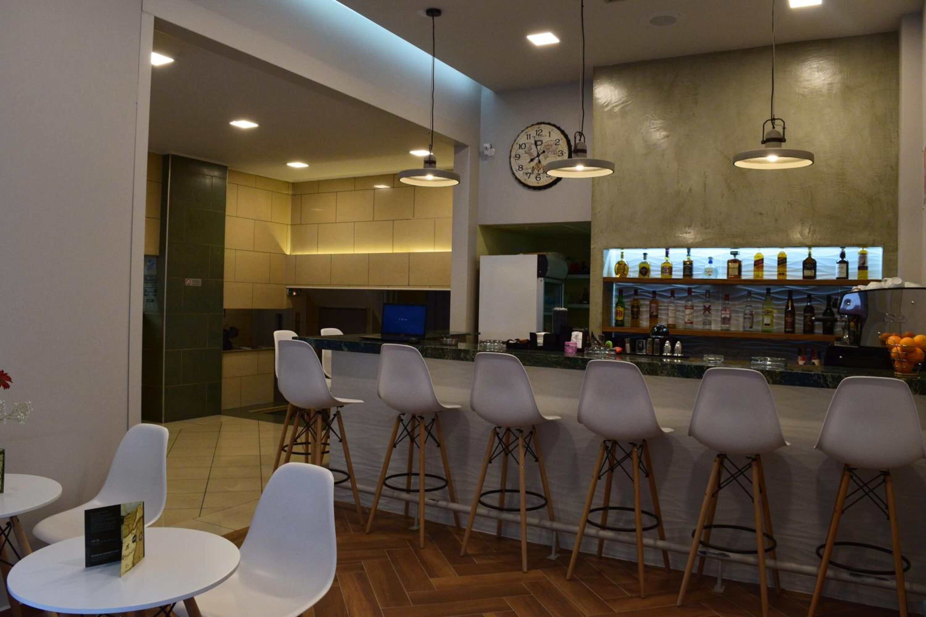 A modern bar area with a clock, bar stools, and a variety of bottles on shelves.