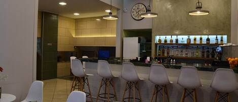 A modern bar area with a clock, bar stools, and a variety of bottles on shelves.