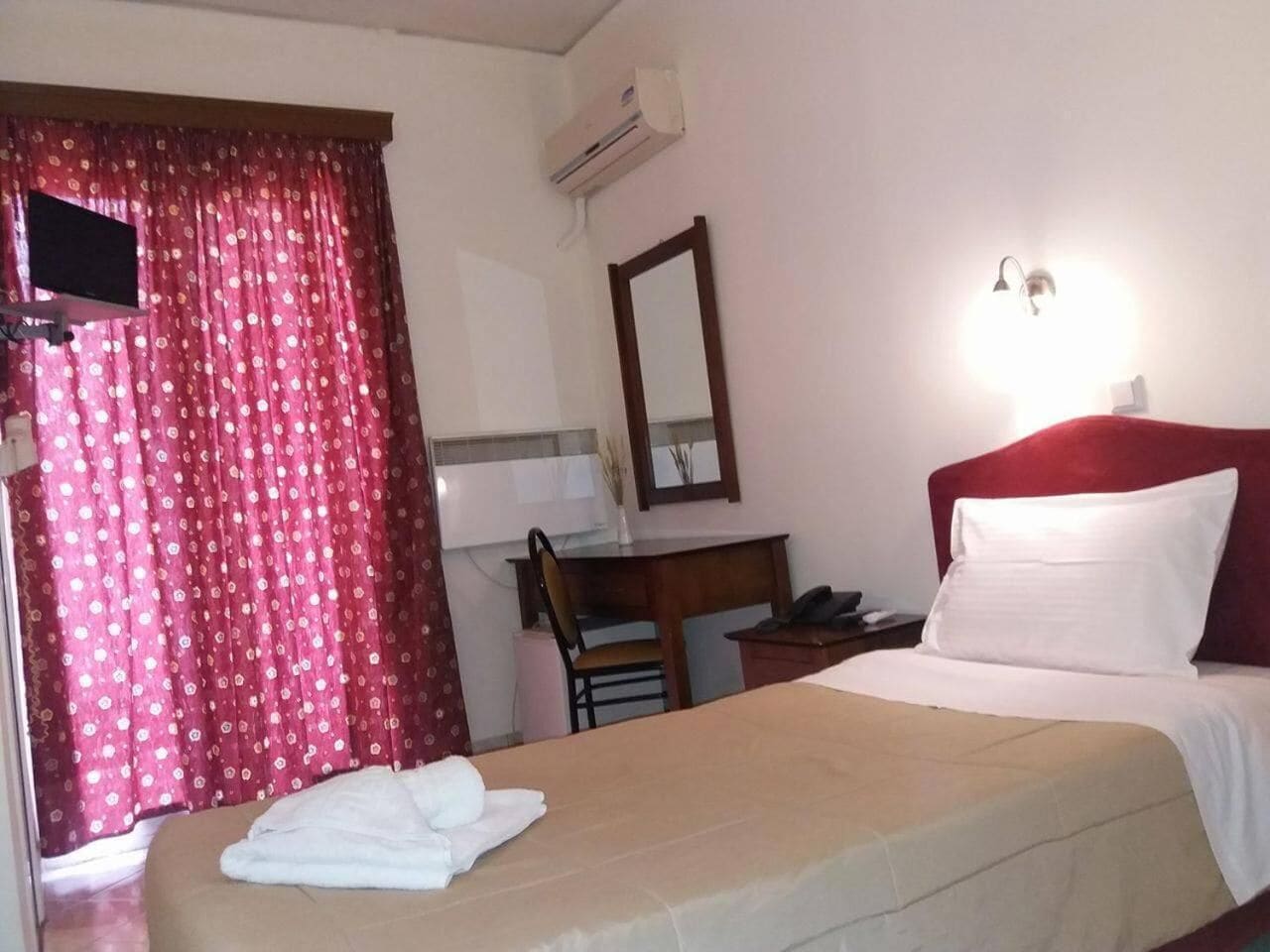 Habitación de hotel con cama, escritorio, silla, espejo y ventana con cortinas.