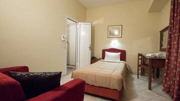 Une chambre d’hôtel avec un lit, un fauteuil rouge, une petite table et une porte.