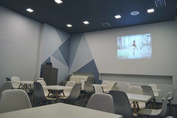 Un salón de conferencias con mesas y sillas, una pantalla mostrando una proyección y un atril.