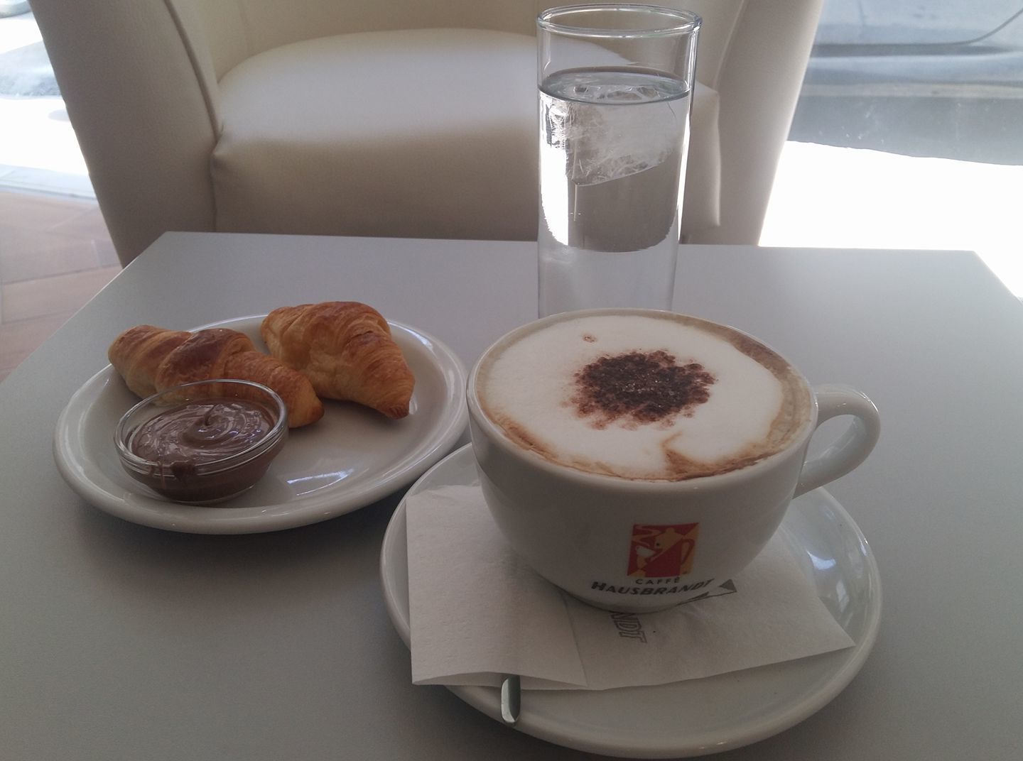 A table with a cup of coffee, croissants, and a glass of water.