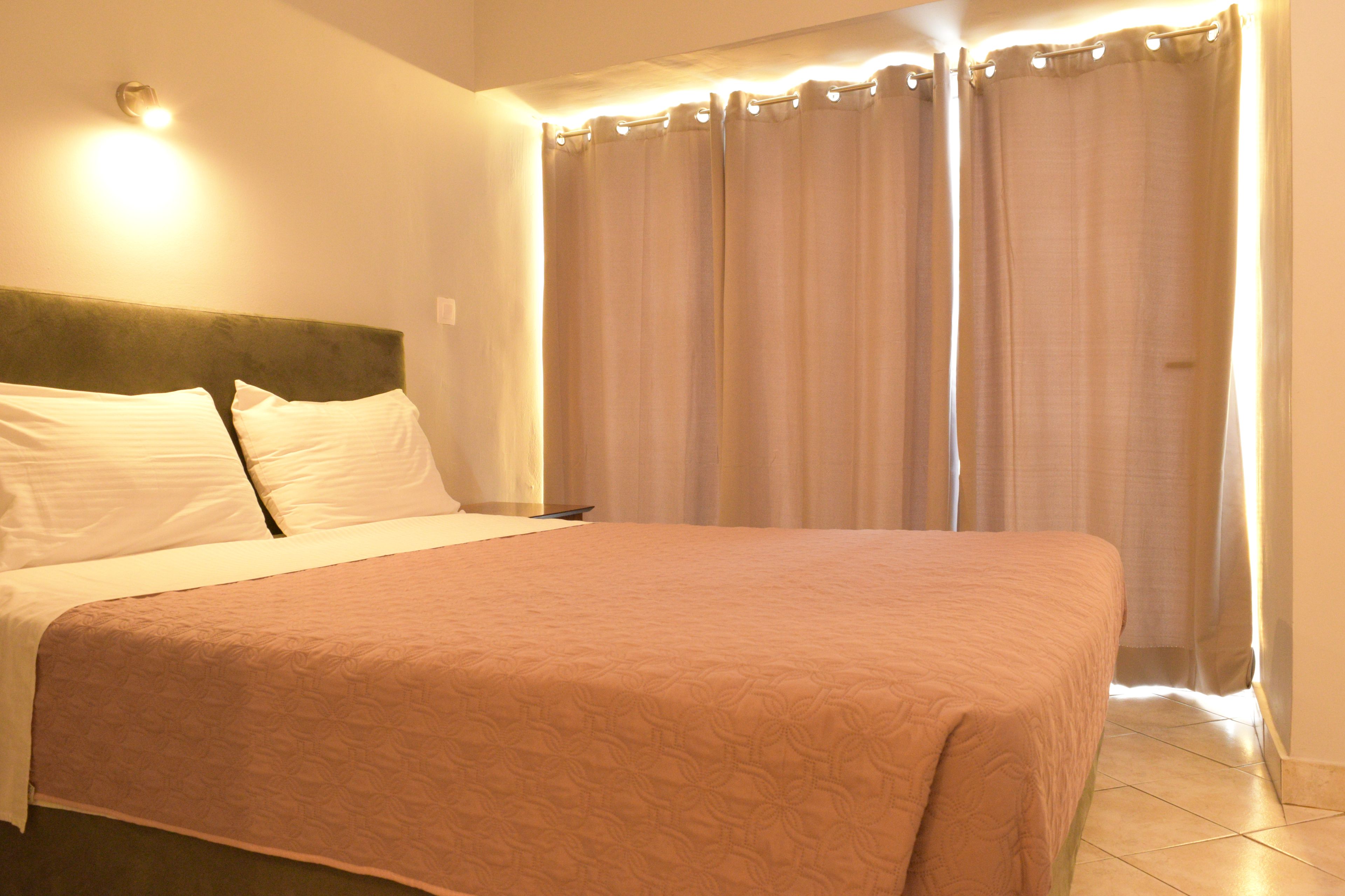 Una cama bien hecha con cabecera, una mesita de noche y una cortina cubriendo la ventana.