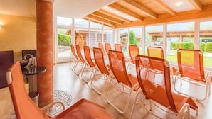 A row of orange chairs with a glass table, wooden beams, and large windows overlooking a garden. - Hotel Kristall (Hermagor-Pressegger See)