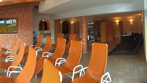 A hotel lobby with rows of orange chairs, a staircase, and a view of the outside. - Hotel Kristall (Hermagor-Pressegger See)