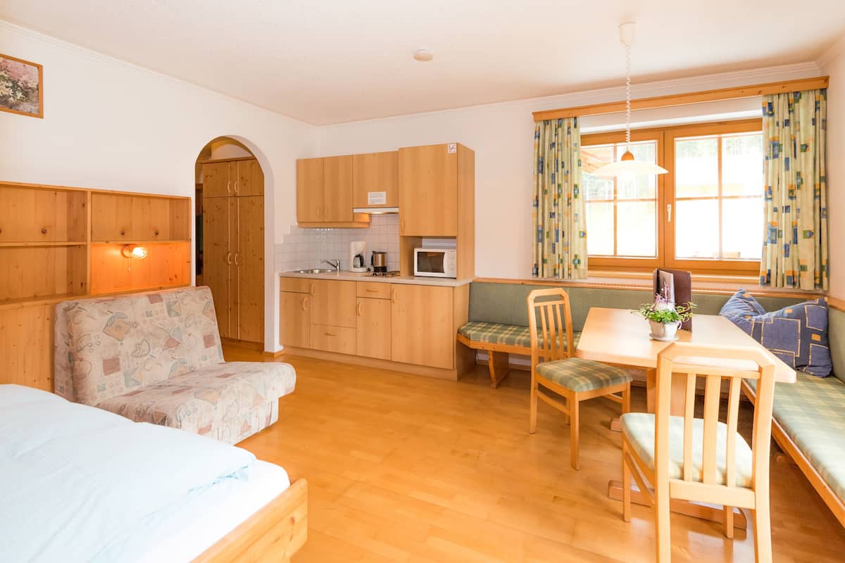 A compact room with a kitchenette, a sofa, a dining table with chairs, and a window with curtains.