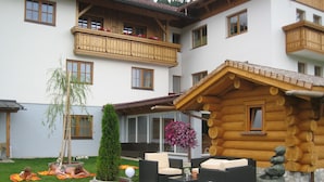 A log cabin with outdoor seating, a small garden, and a multi-story building with balconies. - Hotel Kristall (Hermagor-Pressegger See)