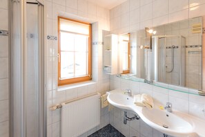 A modern bathroom with a glass shower enclosure, a white sink with a mirror above it, and a window providing natural light.