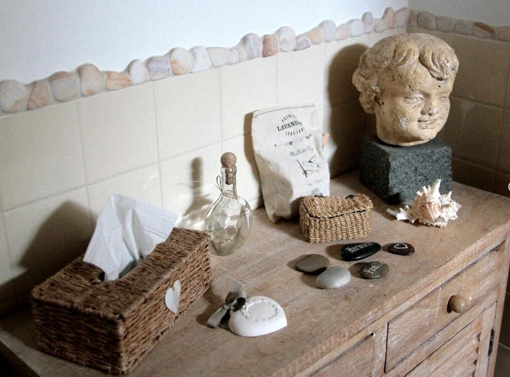 Uma bancada de banheiro com uma escultura de pedra, uma garrafa, um saquinho de lavanda, uma cesta e algumas pedras.