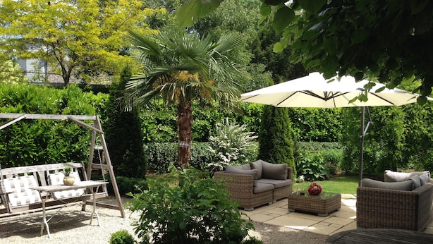 Een tuinpatio met wicker meubilair, een schommel en een pergola.