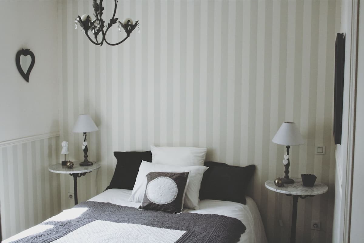 Ein ordentlich eingerichtetes Schlafzimmer mit einem Bett, zwei Nachttischen, einer Chandelüster und einer herzförmigen Dekoration an der Wand.