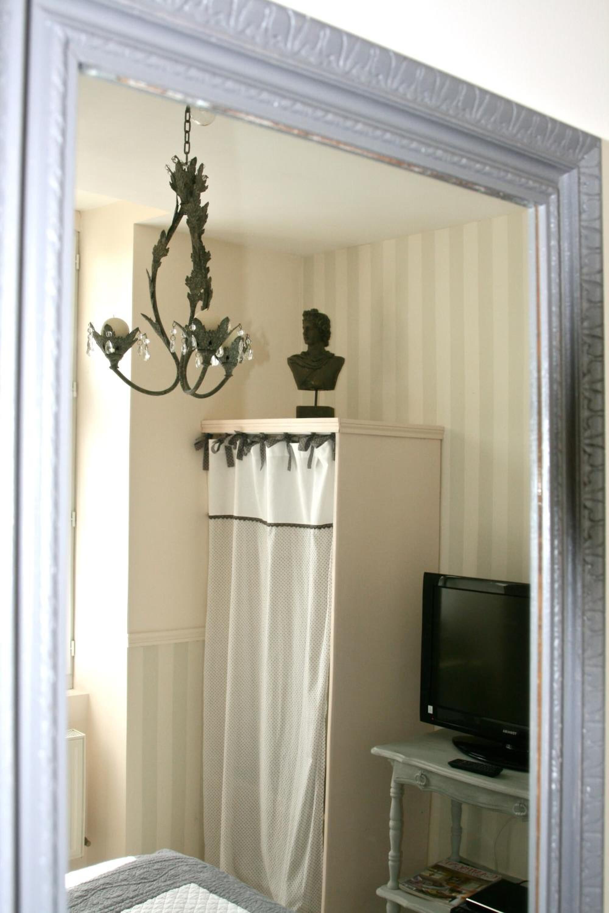 A bedroom with a bed, a television on a small table, a chandelier, and a shower curtain.