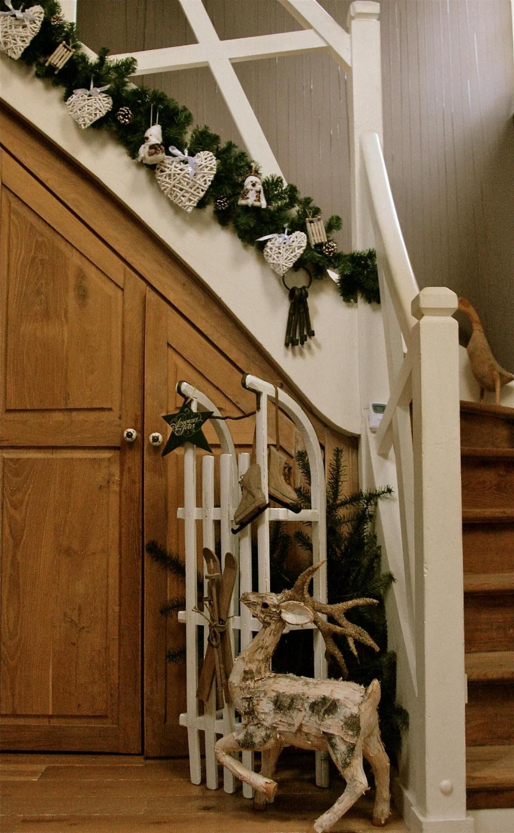 A wooden staircase with a white railing, decorated with Christmas garlands and ornaments.