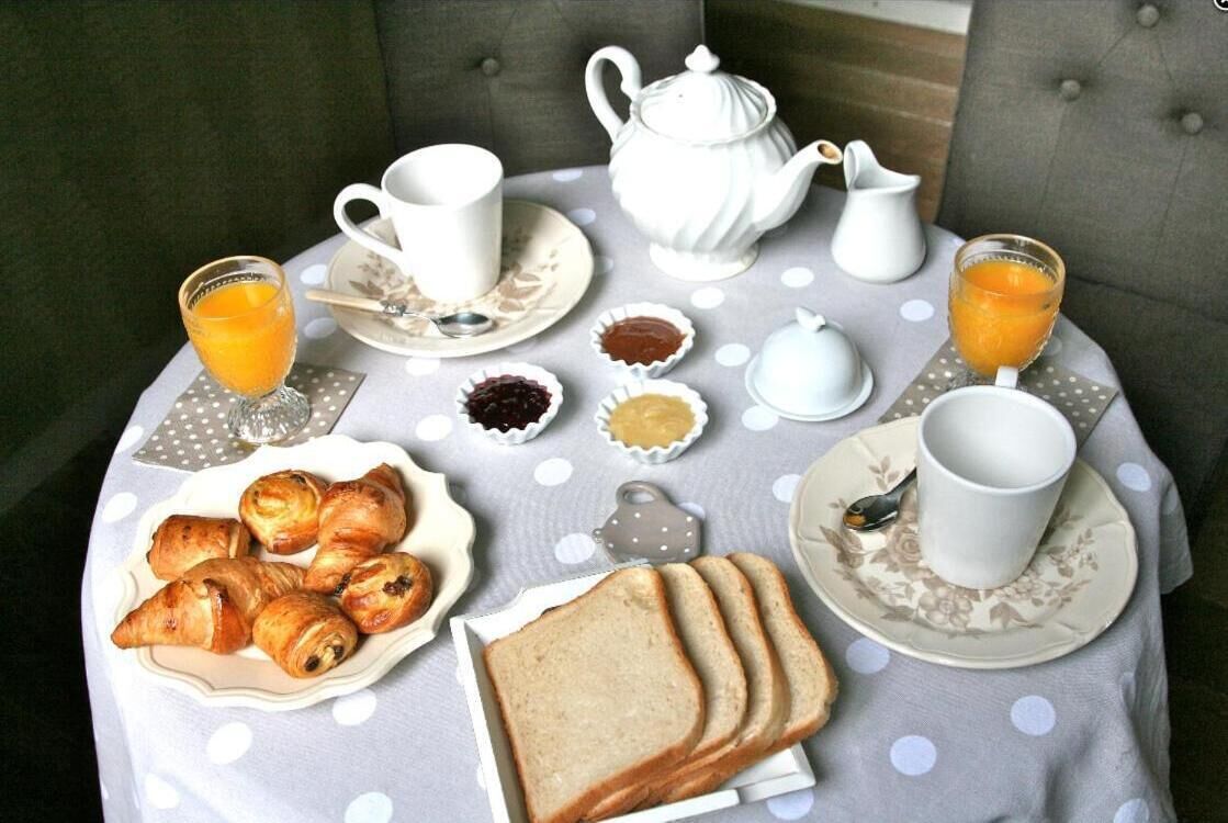 Une table de petit-déjeuner dressée avec des croissants, du pain, de la confiture, du beurre et du jus d’orange.