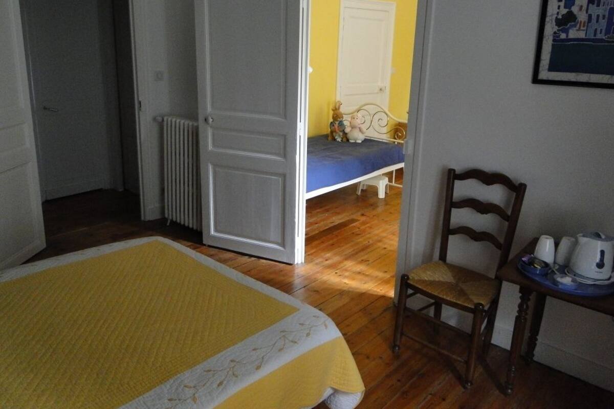 A bedroom with a bed, a chair, a radiator, and a door leading to another room.