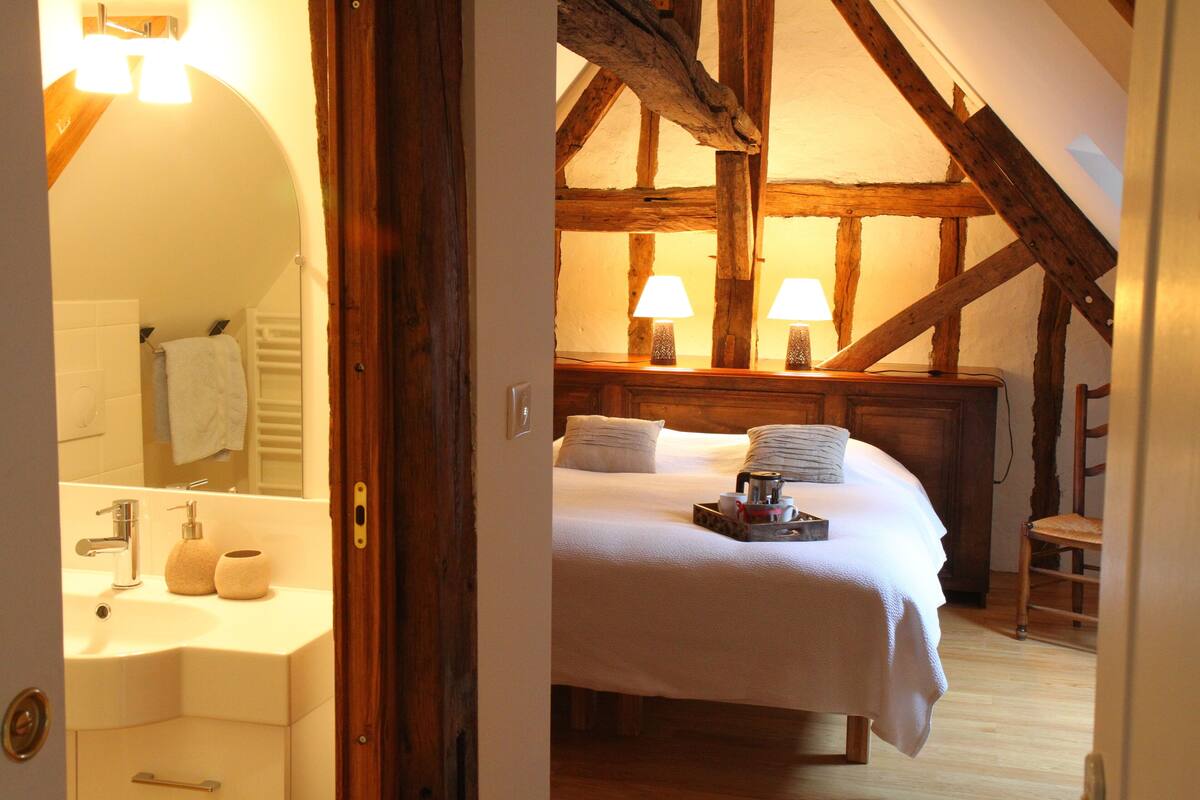 A bedroom with a wooden ceiling, a bed with white bedding, two bedside lamps, and a wooden chair.