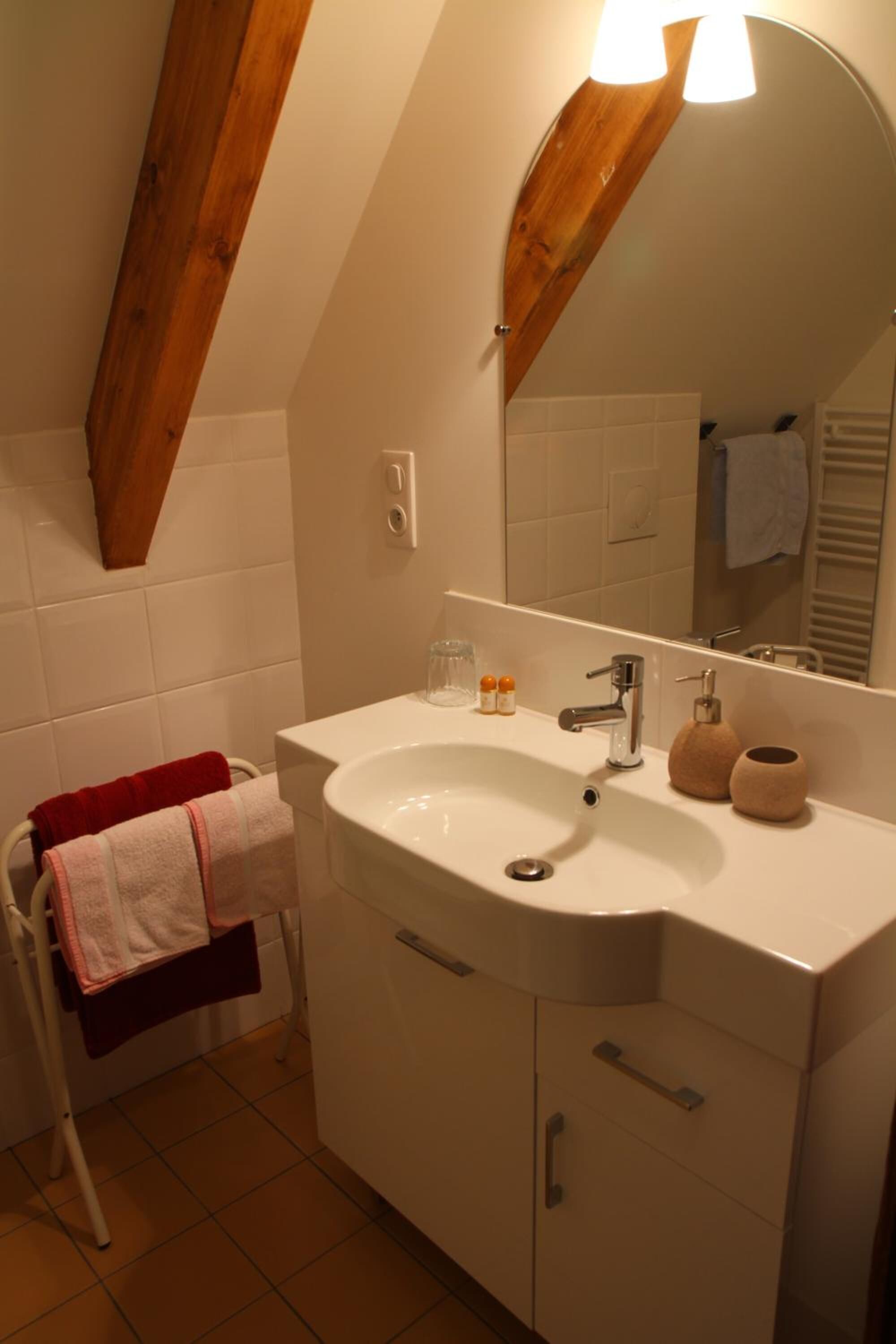 A bathroom with a white sink, mirror, and wooden beams. There is a towel rack with a red towel and a white towel.